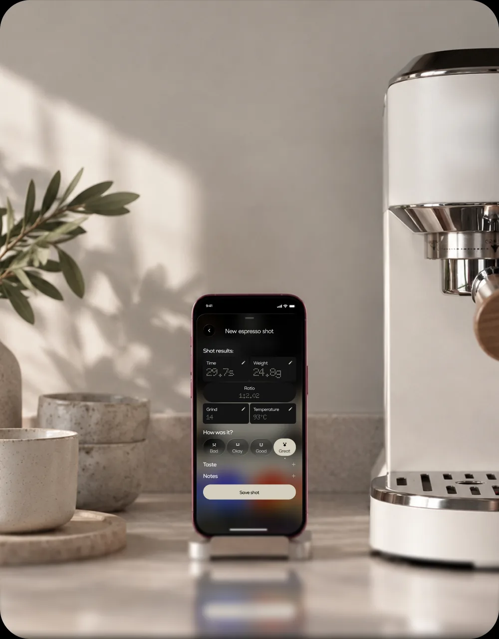 A phone showing the Shot results screen on a kitchen counter next to an espresso machine.